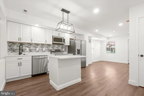 a kitchen with stainless steel appliances kitchen island granite countertop a stove a sink a refrigerator and white cabinets with wooden floor