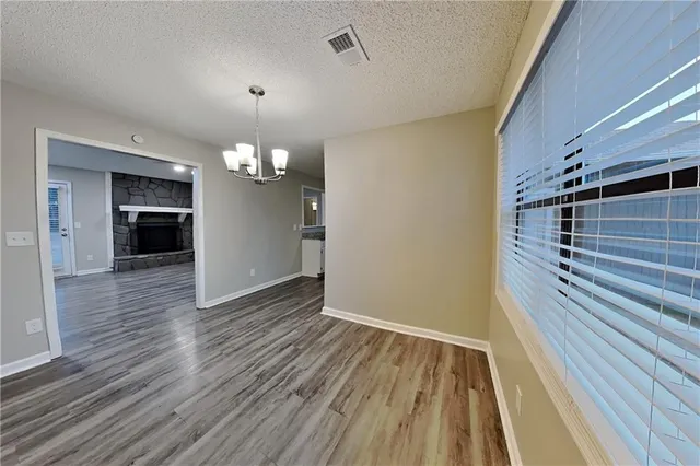 a view of an empty room with wooden floor and kitchen view