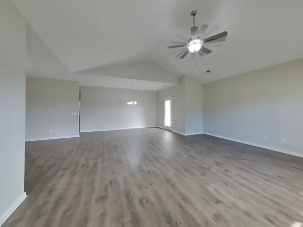 a view of an empty room with wooden floor and a ceiling fan