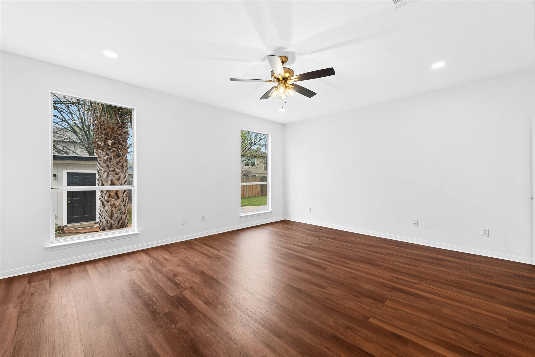 813 Caribou Ridge Trail Pflugerville, TX 78660 - Photo 22 of 39 Unfurnished room featuring a ceiling fan, dark wood-style floors, and recessed lightingSpacious primary bedroom filled with natural light, warm luxury flooring, and large windows showcasing a beautiful mature palm tree view.