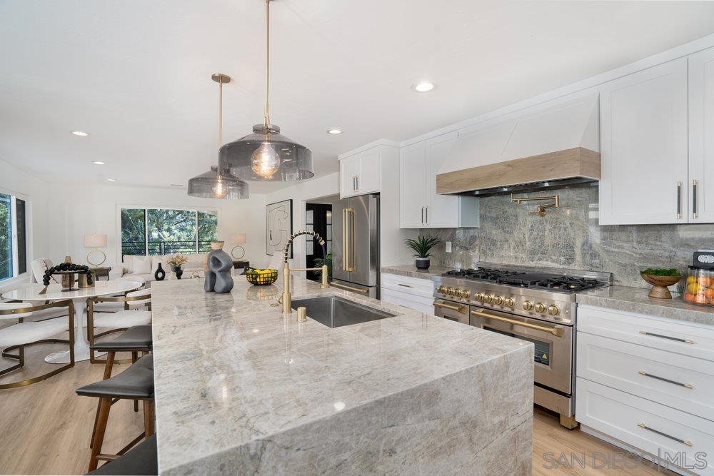a kitchen with stainless steel appliances kitchen island granite countertop a stove a sink a oven a dining table and chairs with white cabinets
