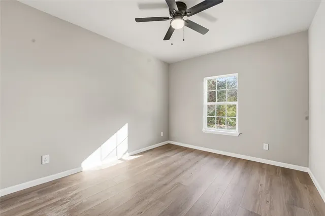 an empty room with wooden floor fan and windows