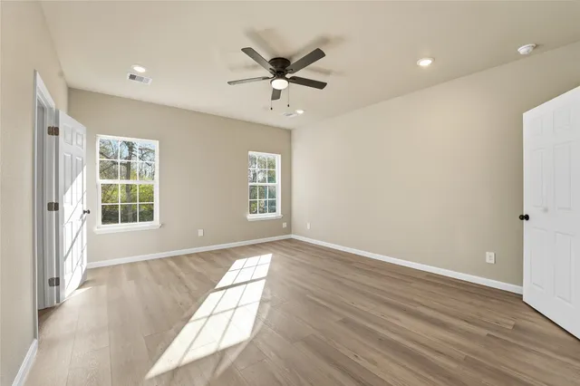 an empty room with wooden floor fan and windows