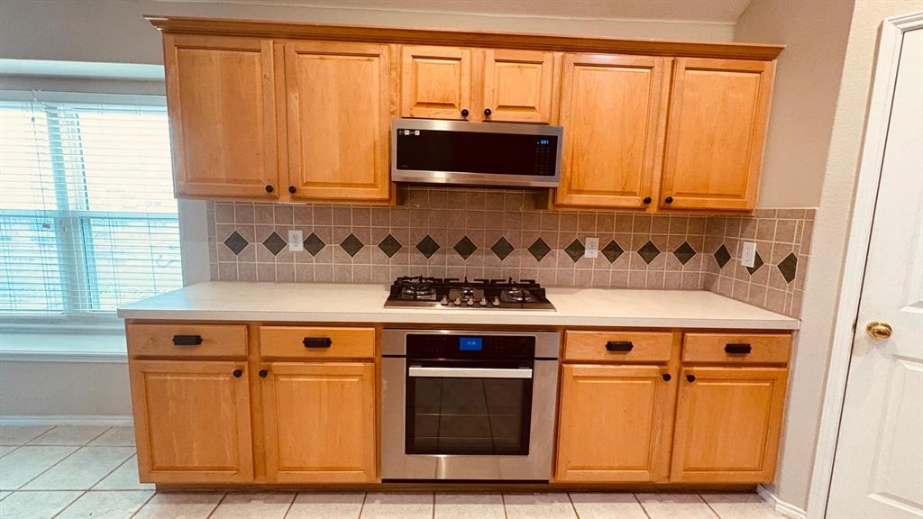 5970 Dustin Trail Frisco, TX 75034 - Photo 12 of 31 Kitchen featuring light wood cabinetry, light-colored countertops, a tile backsplash with decorative accents, stainless steel oven, and a gas cooktop