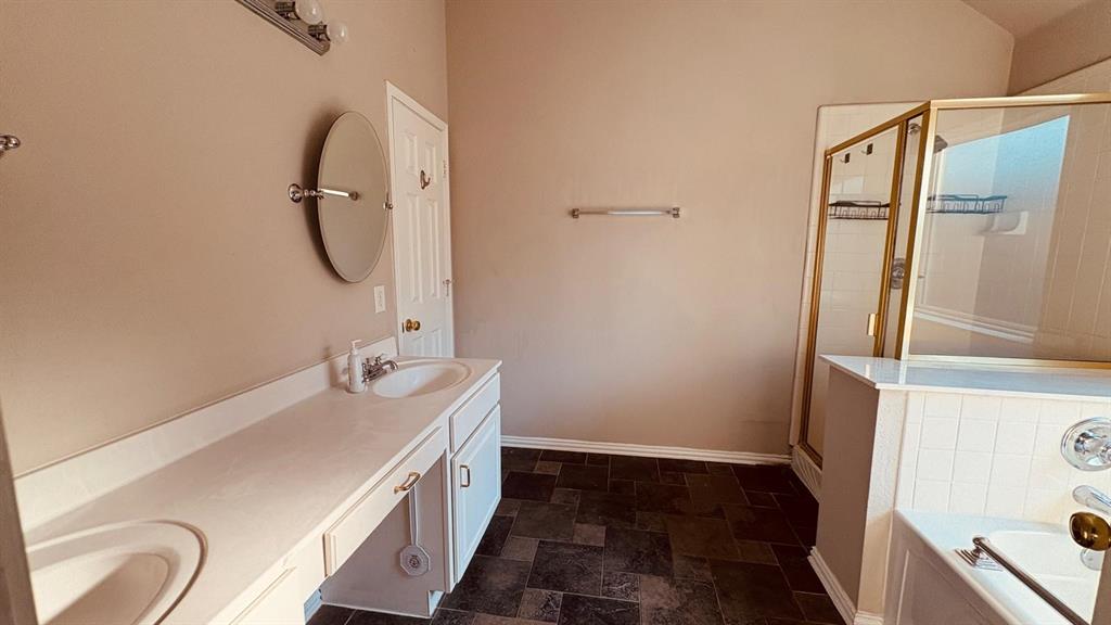 5970 Dustin Trail Frisco, TX 75034 - Photo 20 of 31 Bathroom featuring a dual vanity with integrated sinks, a built-in bathtub with white subway tile surround, a shower with a gold-tone framed glass enclosure, a wall-mounted cosmetic mirror, and dark tile flooring