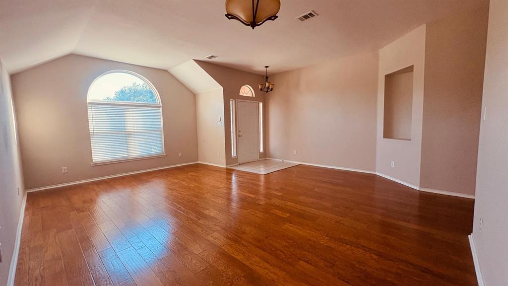 5970 Dustin Trail Frisco, TX 75034 - Photo 7 of 31 Spacious room featuring vaulted ceilings, a large arched window with blinds, wood-finish flooring, a built-in wall niche, and a neutral color palette