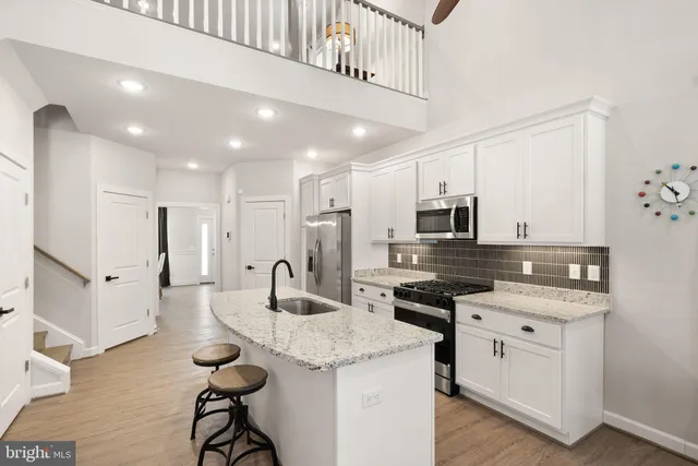 a kitchen with stainless steel appliances kitchen island granite countertop a refrigerator a stove and white cabinets with wooden floors