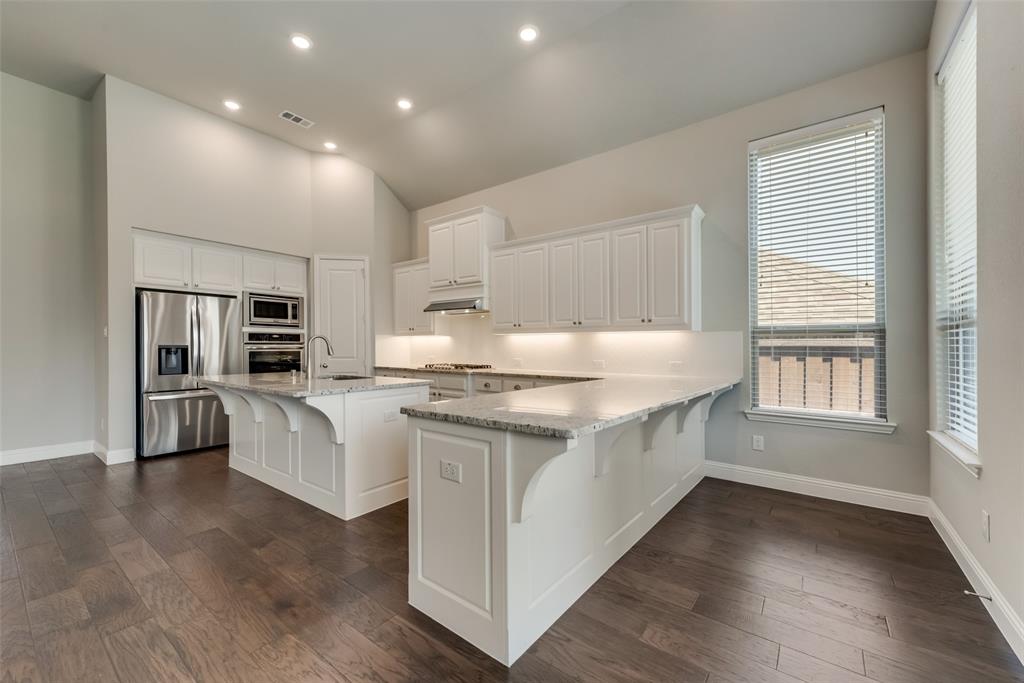 3916 Ironbark Way McKinney, TX 75071 - Photo 8 of 23 a large white kitchen with kitchen island white cabinets and stainless steel appliances