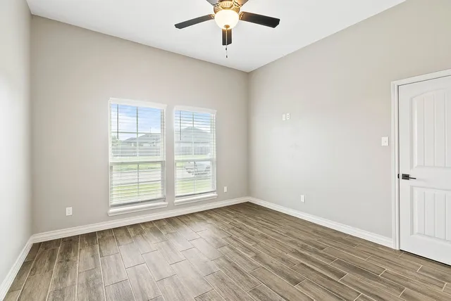 an empty room with wooden floor chandelier fan and windows