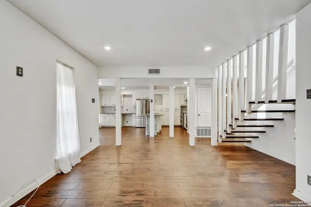 a view of an empty room with wooden floor and stairs