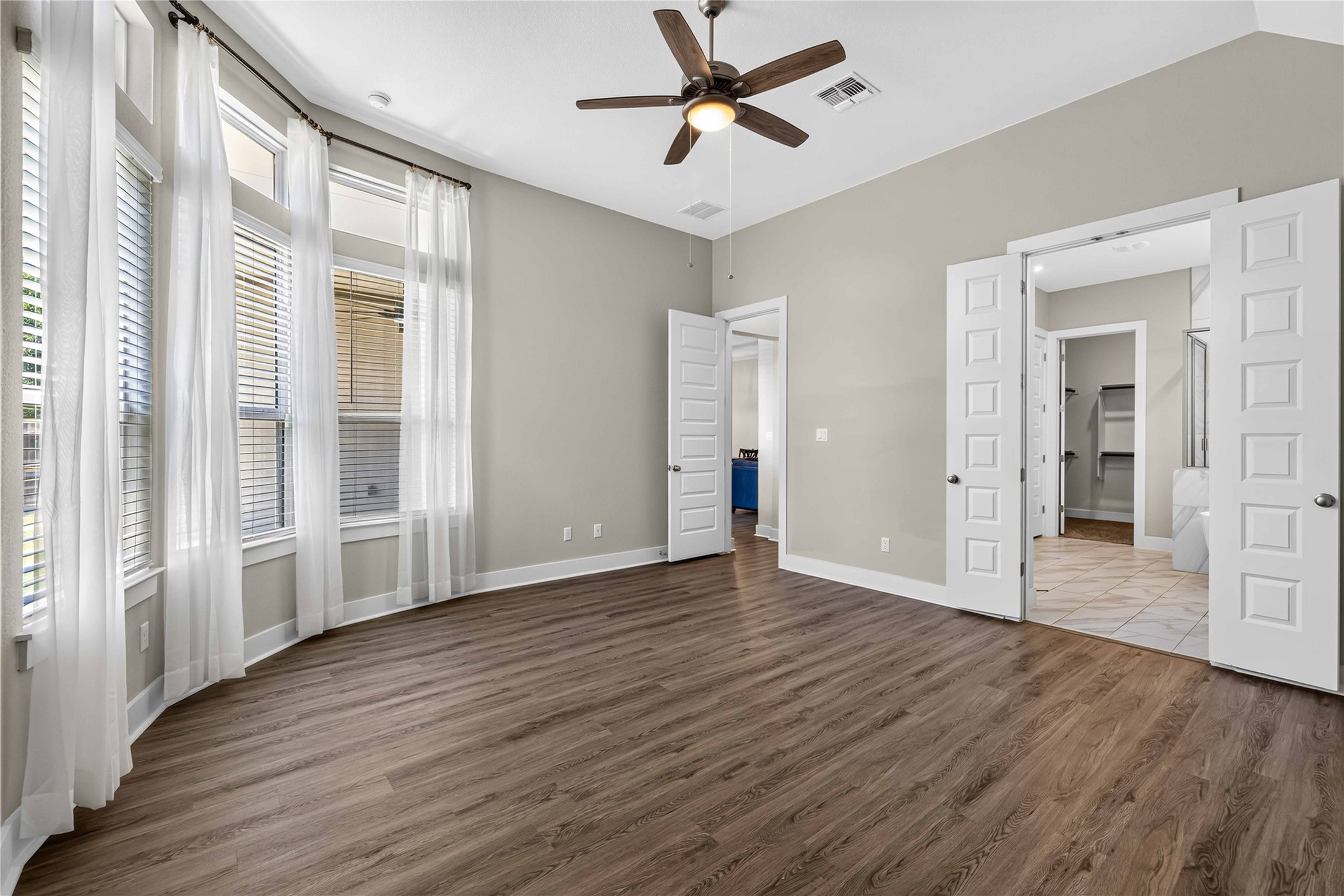 605 A Mallow Road Leander, TX 78641 - Photo 13 of 29 A gracefully curved wall of windows illuminates this primary bedroom, featuring rich wood flooring and a classic ceiling fan.
