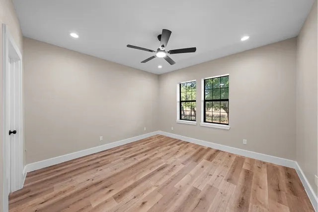an empty room with wooden floor fan and windows