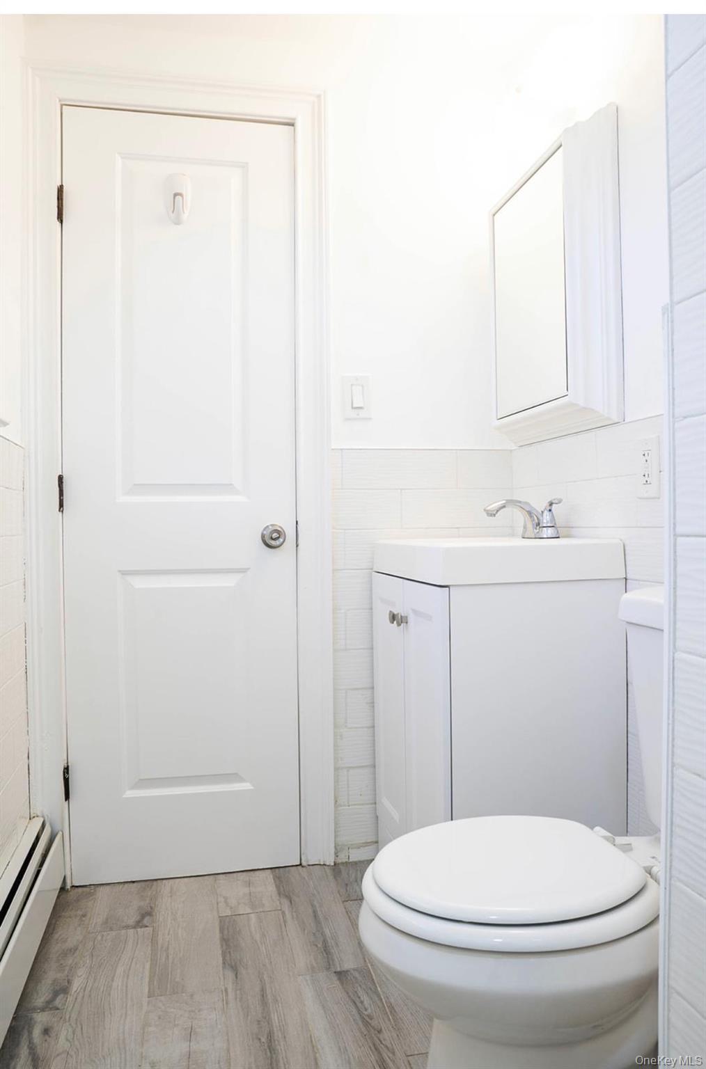 58 Hauppauge Road Hauppauge, NY 11788 - Photo 26 of 34 Half bath featuring tile walls, vanity, light wood-style flooring, a baseboard heating unit, and wainscoting