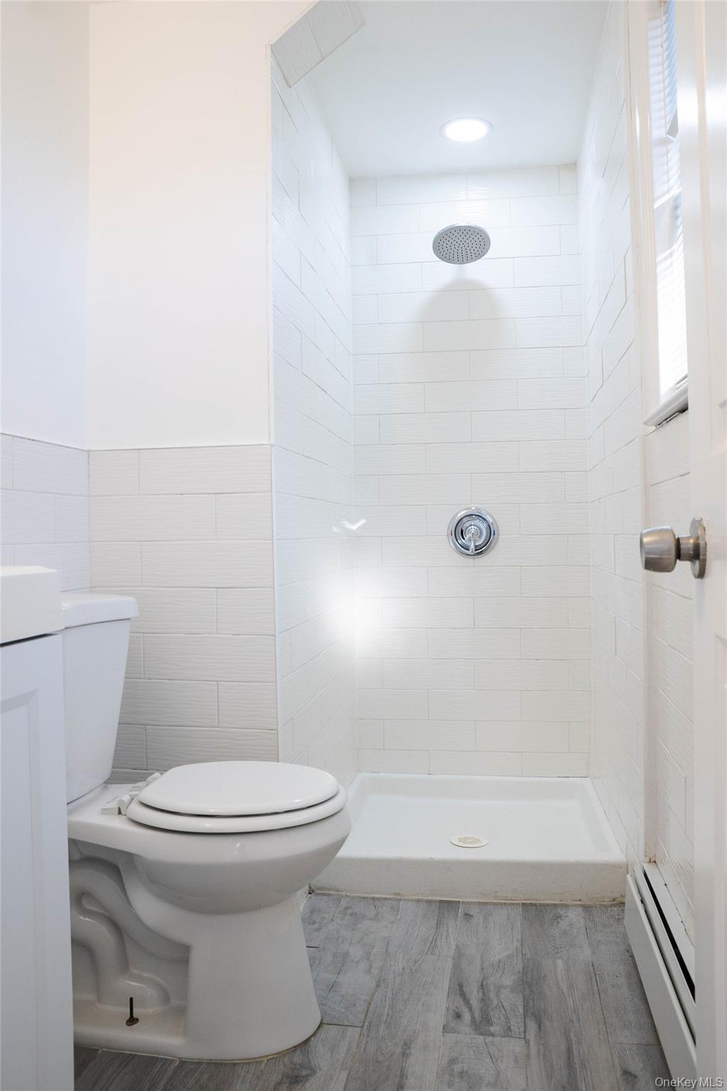 58 Hauppauge Road Hauppauge, NY 11788 - Photo 27 of 34 Full bathroom with baseboard heating, a stall shower, light wood-type flooring, tile walls, and vanity