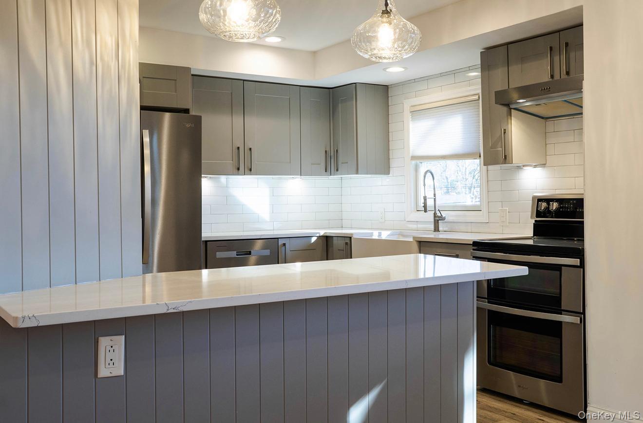 58 Hauppauge Road Hauppauge, NY 11788 - Photo 4 of 34 Kitchen with stainless steel appliances, gray cabinets, under cabinet range hood, a center island, and hanging light fixtures