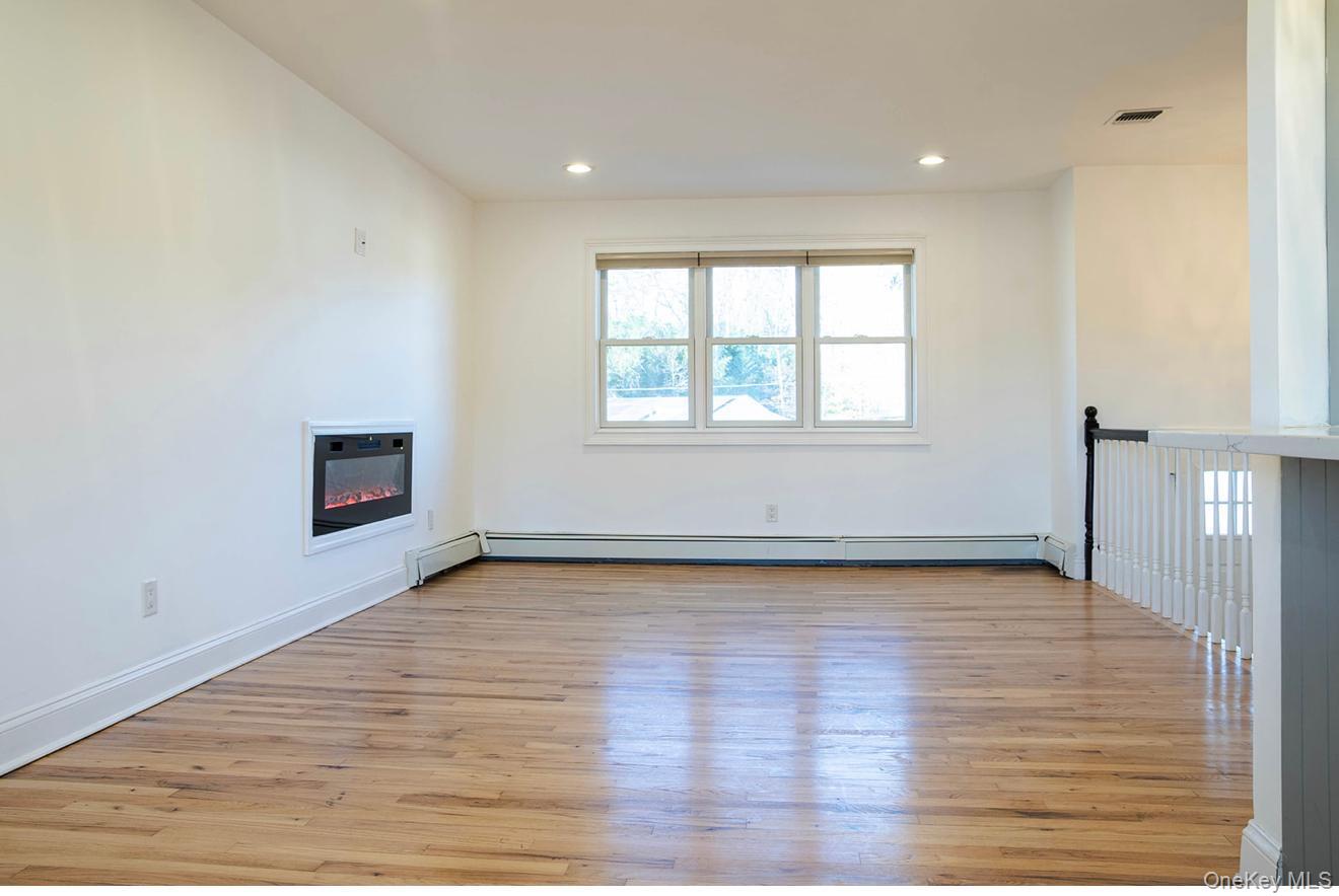58 Hauppauge Road Hauppauge, NY 11788 - Photo 9 of 34 Unfurnished living room with a glass covered fireplace, light wood-style flooring, recessed lighting, and baseboard heating