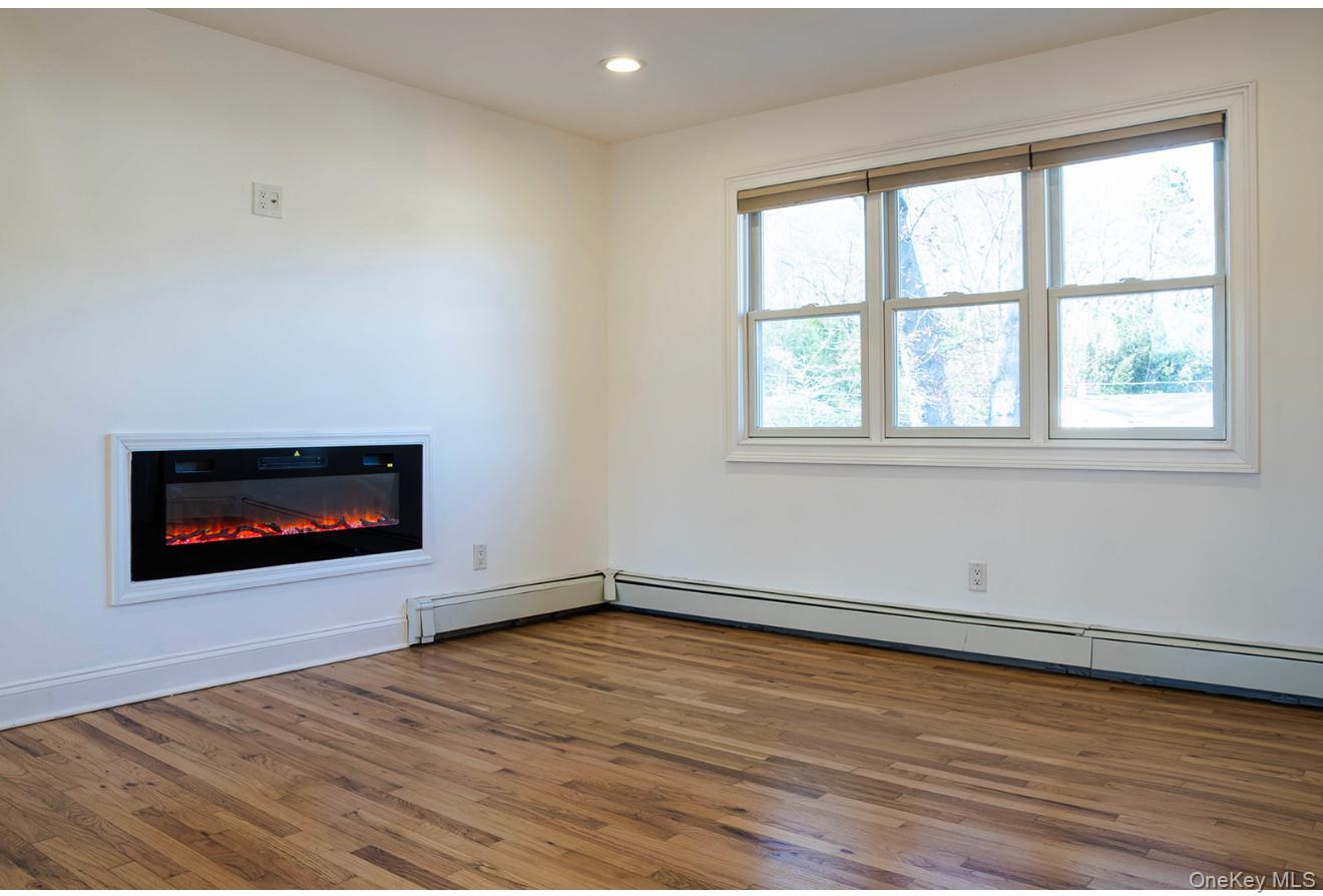 58 Hauppauge Road Hauppauge, NY 11788 - Photo 10 of 34 Unfurnished living room featuring a glass covered fireplace, wood-type flooring, recessed lighting, and a baseboard heating unit