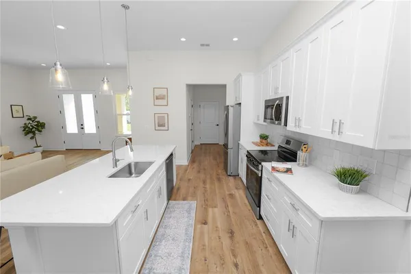 a kitchen with stainless steel appliances white cabinets a sink a stove a microwave and wooden floors