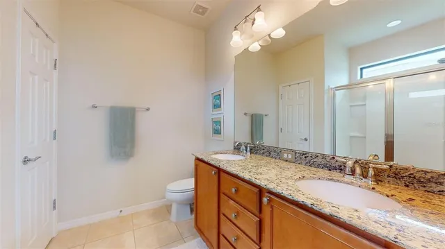 a bathroom with a granite countertop double vanity sink a toilet and a mirror