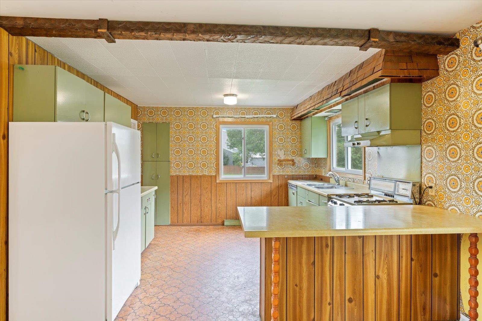 202 Suffolk Drive Hoyt Lakes, MN 55750 - Photo 11 of 33 Kitchen featuring wallpapered walls, freestanding refrigerator, a peninsula, green cabinetry, and wooden walls