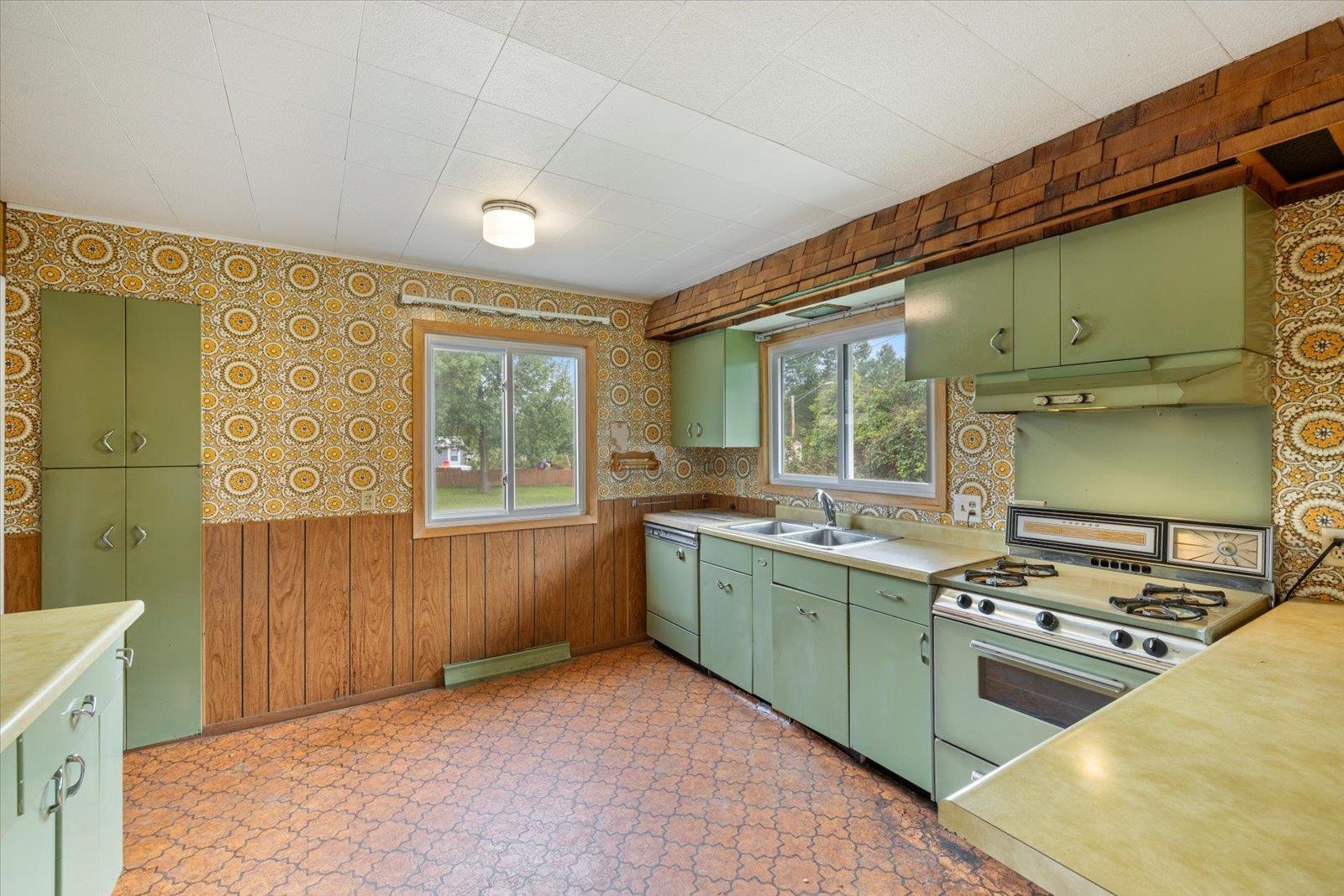 202 Suffolk Drive Hoyt Lakes, MN 55750 - Photo 12 of 33 Kitchen with green cabinets, wallpapered walls, a wainscoted wall, plenty of natural light, and white appliances