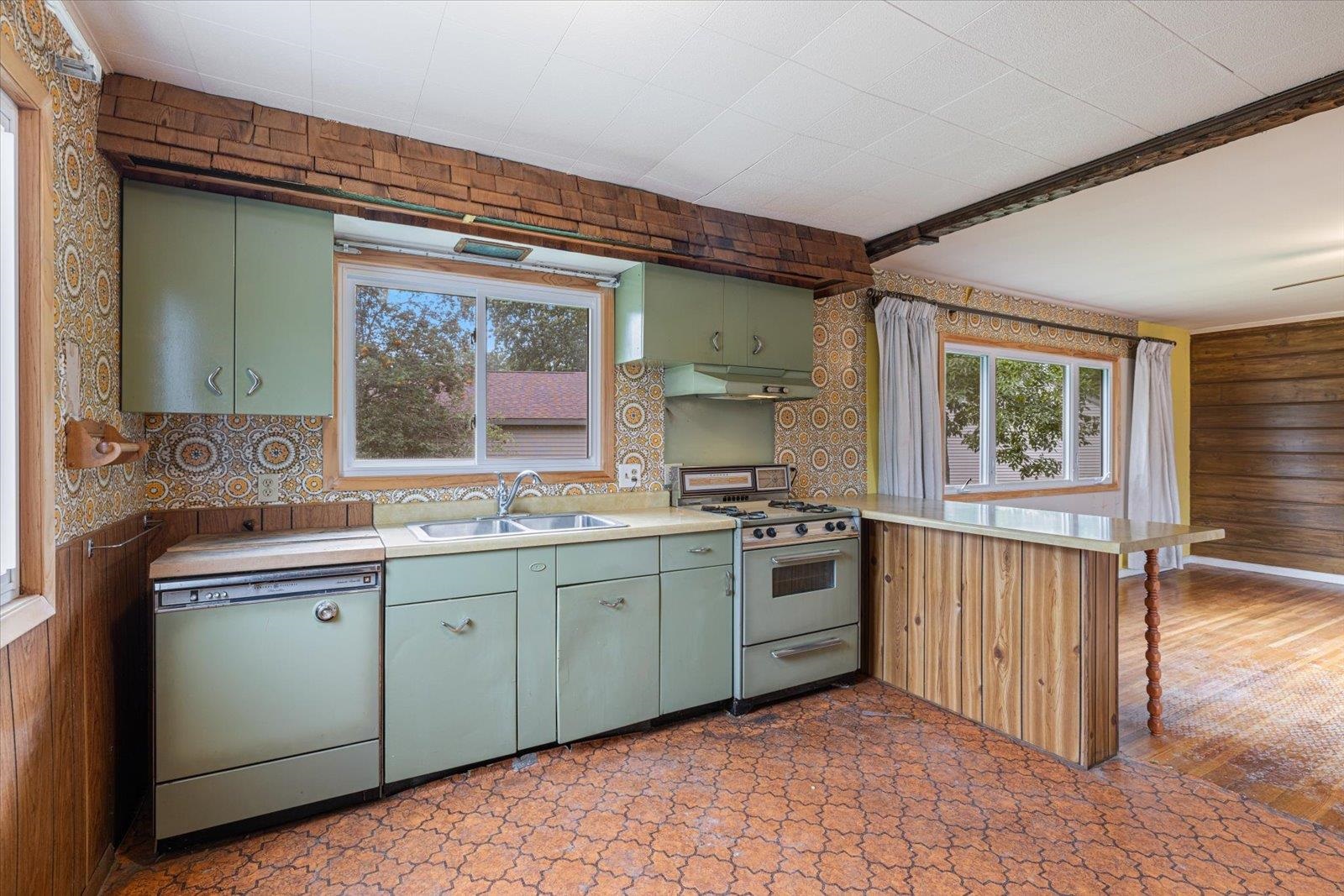 202 Suffolk Drive Hoyt Lakes, MN 55750 - Photo 14 of 33 Kitchen with green cabinets, a peninsula, white appliances, light countertops, and wooden walls