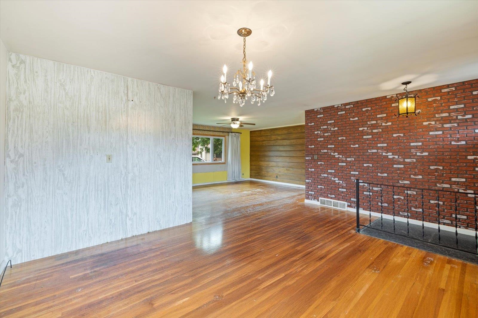 202 Suffolk Drive Hoyt Lakes, MN 55750 - Photo 8 of 33 Unfurnished living room with dark wood finished floors, a ceiling fan, a chandelier, wooden walls, and brick wall