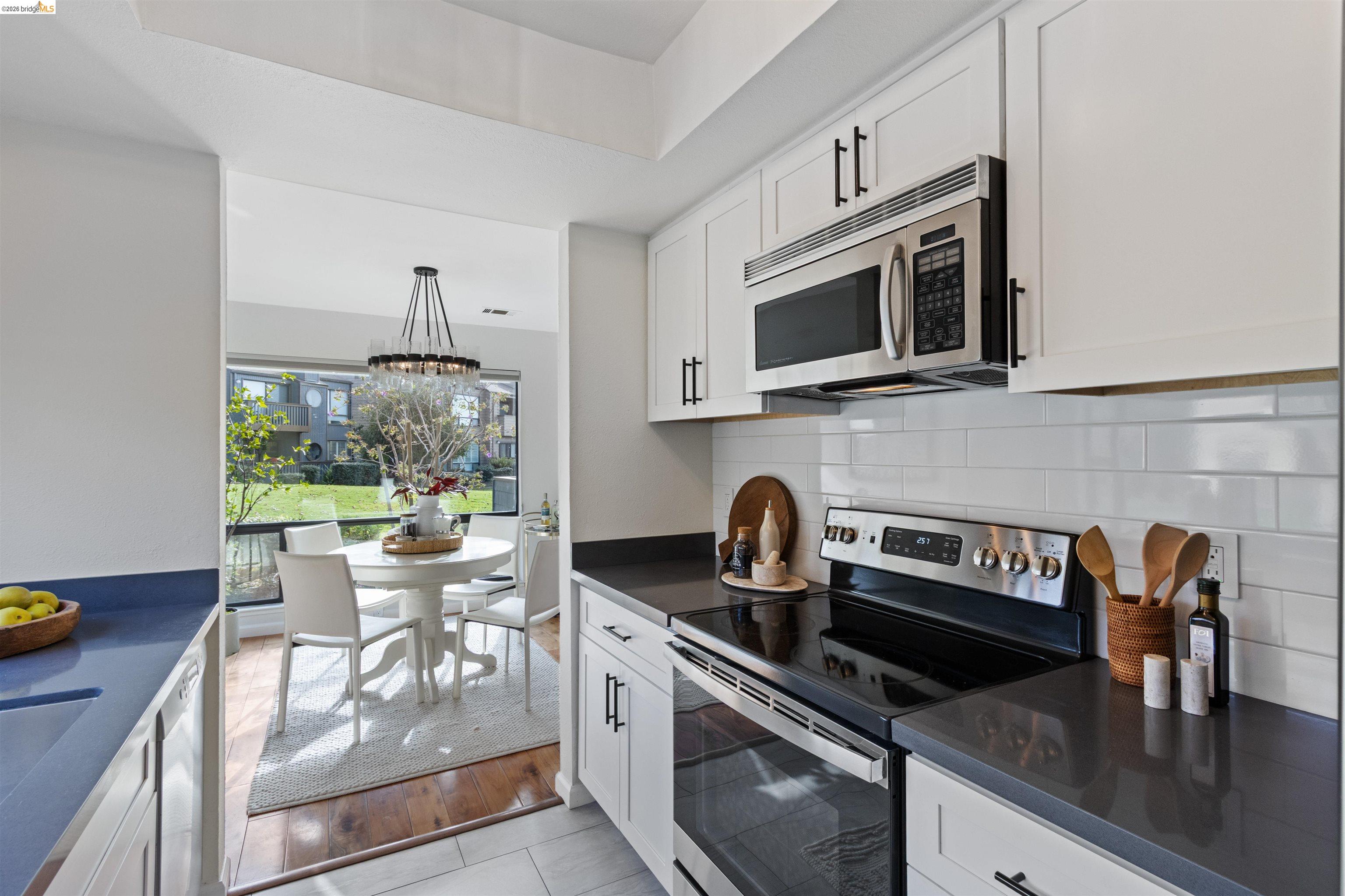548 Queen's Road Alameda, CA 94501 - Photo 11 of 42 Kitchen featuring dark countertops, stainless steel appliances, white cabinetry, decorative backsplash, and hanging light fixtures