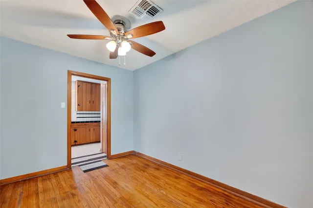 an empty room with wooden floor ceiling fan and windows