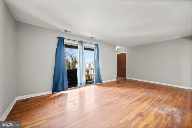 a view of an empty room with wooden floor and kitchen