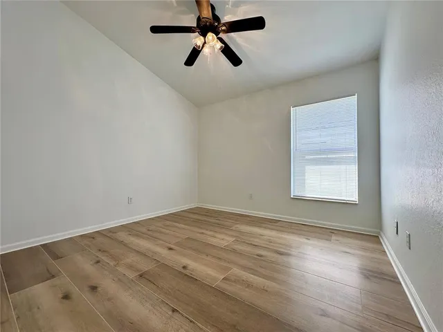 an empty room with wooden floor ceiling fan and windows