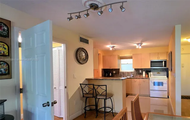 a kitchen with stainless steel appliances kitchen island granite countertop a refrigerator a stove and a dining table with wooden floor