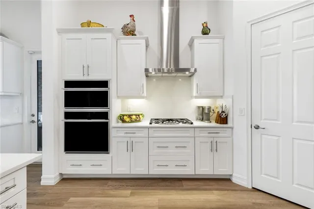 a large white kitchen with a large island oven a sink dishwasher a stove and a dining table with wooden floor