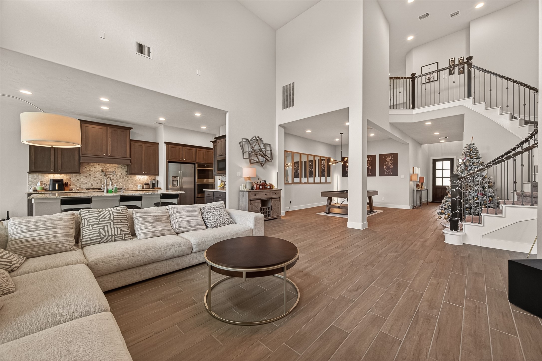 1815 Brea Rdg Trail Katy, TX 77494 - Photo 43 of 43 This spacious living area features high ceilings and an open floor plan, seamlessly connecting to a modern kitchen with dark wood cabinets and a large island. The space includes elegant wood flooring, a cozy sectional sofa, and a stylish staircase leading to the upper level. Ideal for entertaining and family living.