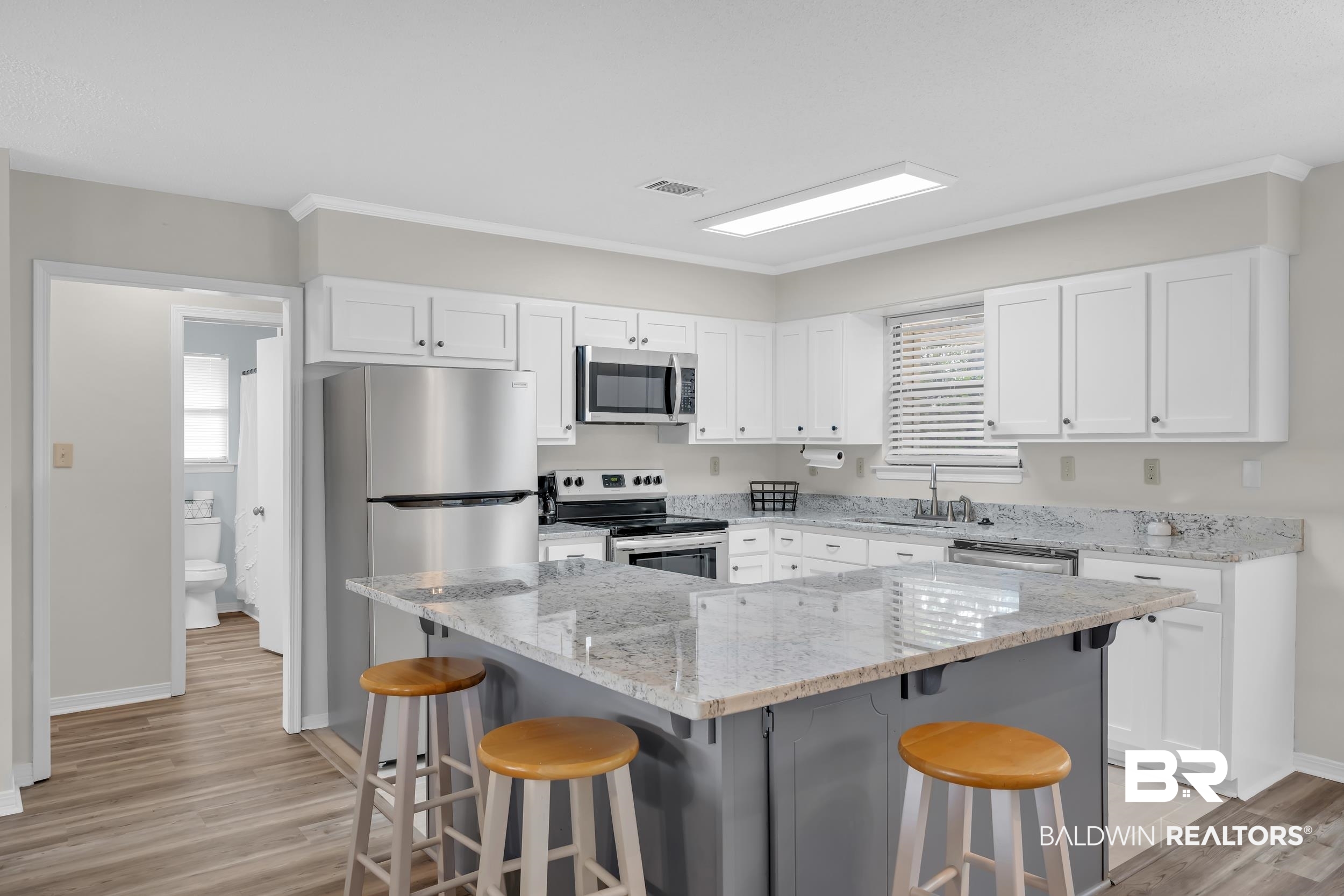 8081 Bryant's Lndg Road Stockton, AL 36579 - Photo 22 of 48 Dual tone kitchen featuring light stone counters, a kitchen breakfast bar, stainless steel appliances, light wood-style floors, and crown molding