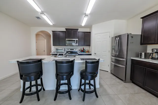 a kitchen with stainless steel appliances a sink a stove a refrigerator dining table and chairs