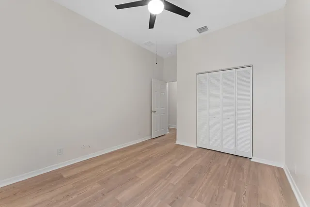 an empty room with wooden floor ceiling fan and windows