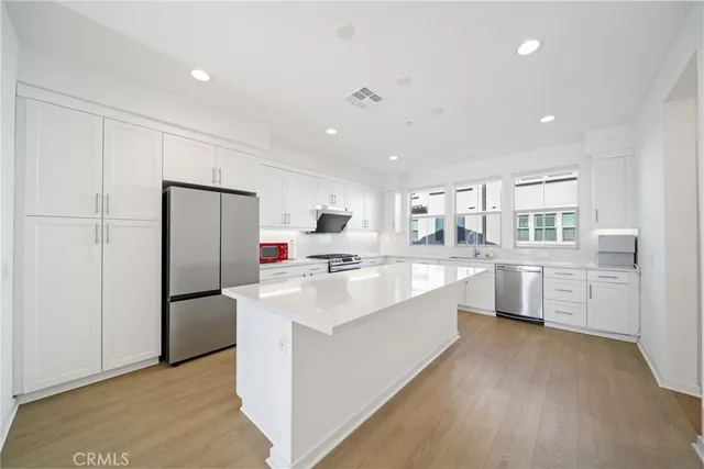 a large white kitchen with a refrigerator a sink dishwasher and a stove with wooden floor