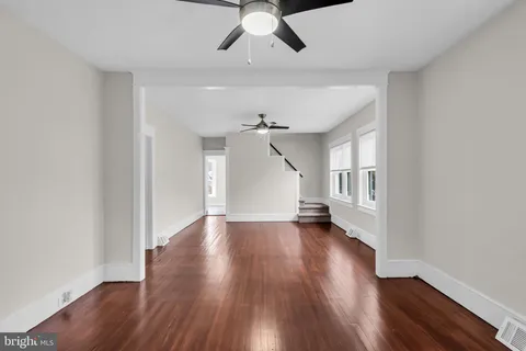 an empty room with wooden floor chandelier fan and windows