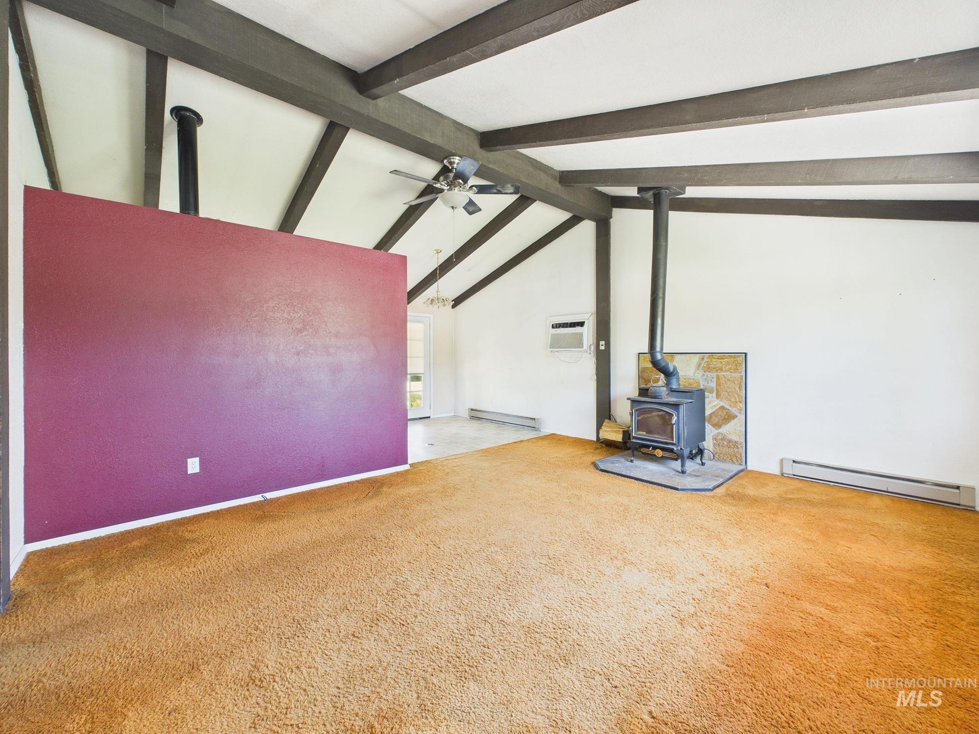 1527 North Plaza Road Emmett, ID 83617 - Photo 4 of 33 Vaulted ceiling with exposed beams, wood-burning stove with stone surround, wall-mounted air conditioning unit, and plush carpeting