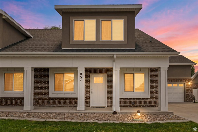 857 225 South Springville, UT 84663 - Photo 17 of 23 Brick and stucco exterior featuring a covered porch with white columns, a prominent second-story dormer with multiple windows, an attached garage, and a manicured lawn