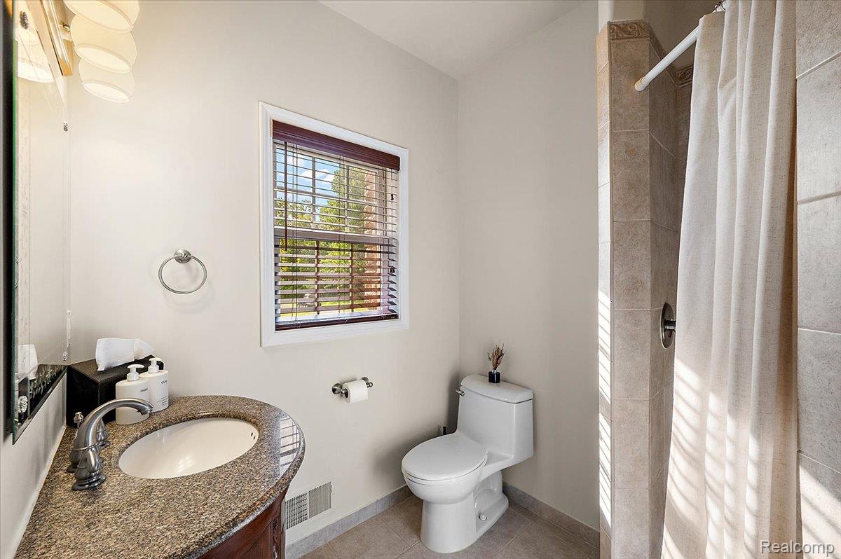 5035 Hidden Ridge Road Metamora, MI 48455 - Photo 17 of 62 Bathroom featuring a curved vanity with a granite countertop and undermount sink, a tiled shower, and a window with wood blinds