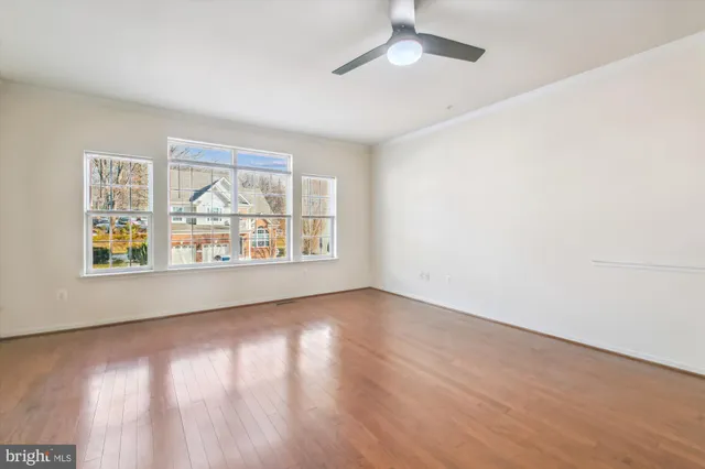 an empty room with wooden floor chandelier fan and windows