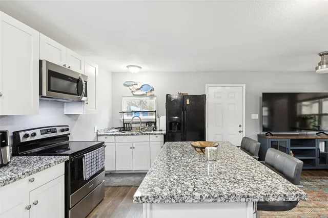 a kitchen with stainless steel appliances granite countertop a stove top oven a sink dishwasher and white cabinets with wooden floor