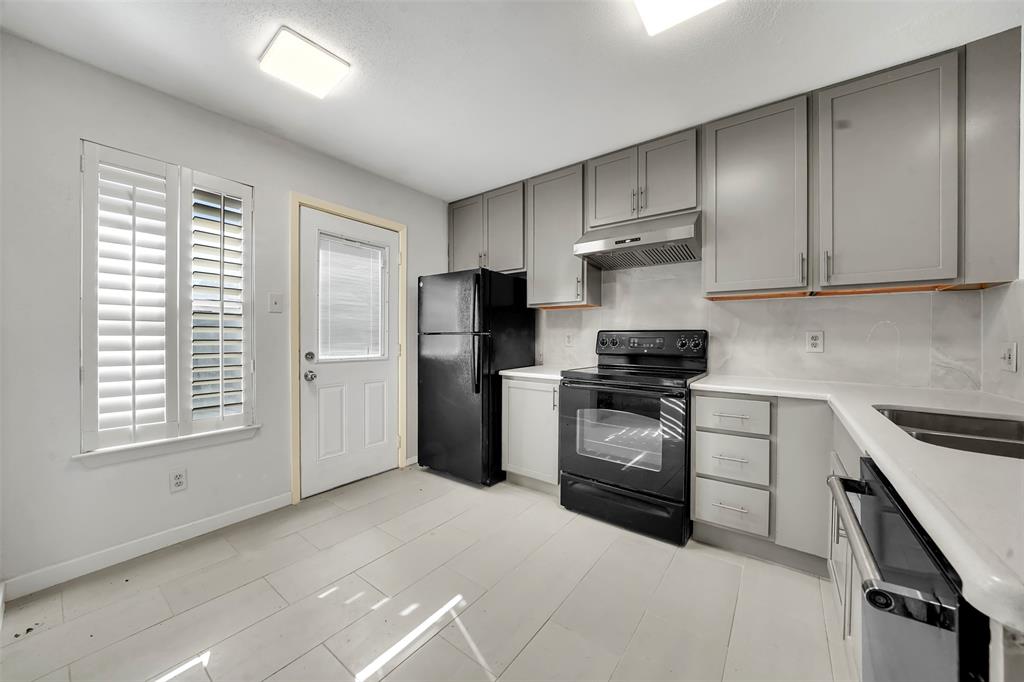 2111 East Belt Line Road, Unit 166B Richardson, TX 75081 - Photo 5 of 23 Kitchen featuring gray cabinetry, black appliances, under cabinet range hood, light stone counters, and tasteful backsplash