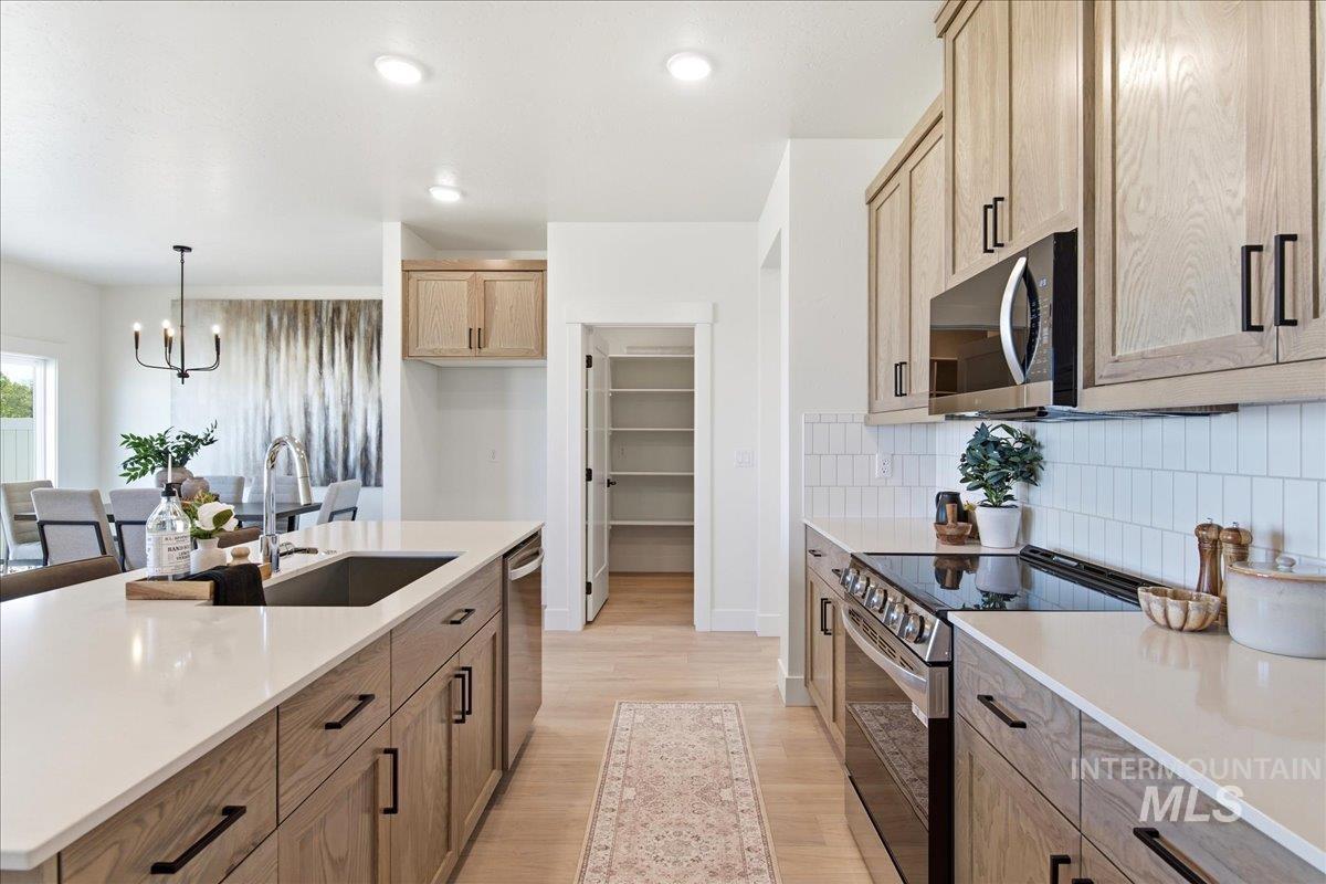 3405 Elliptical Lane Caldwell, ID 83607 - Photo 6 of 17 Modern kitchen featuring light wood-finish cabinetry, white countertops, a stainless steel appliance suite, and a pantry with built-in shelving
