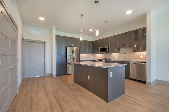 a kitchen with stainless steel appliances granite countertop a refrigerator a sink dishwasher and a oven with wooden floor