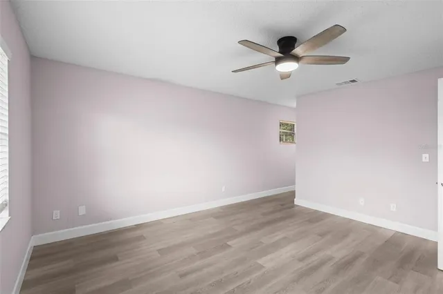 an empty room with wooden floor fan and windows