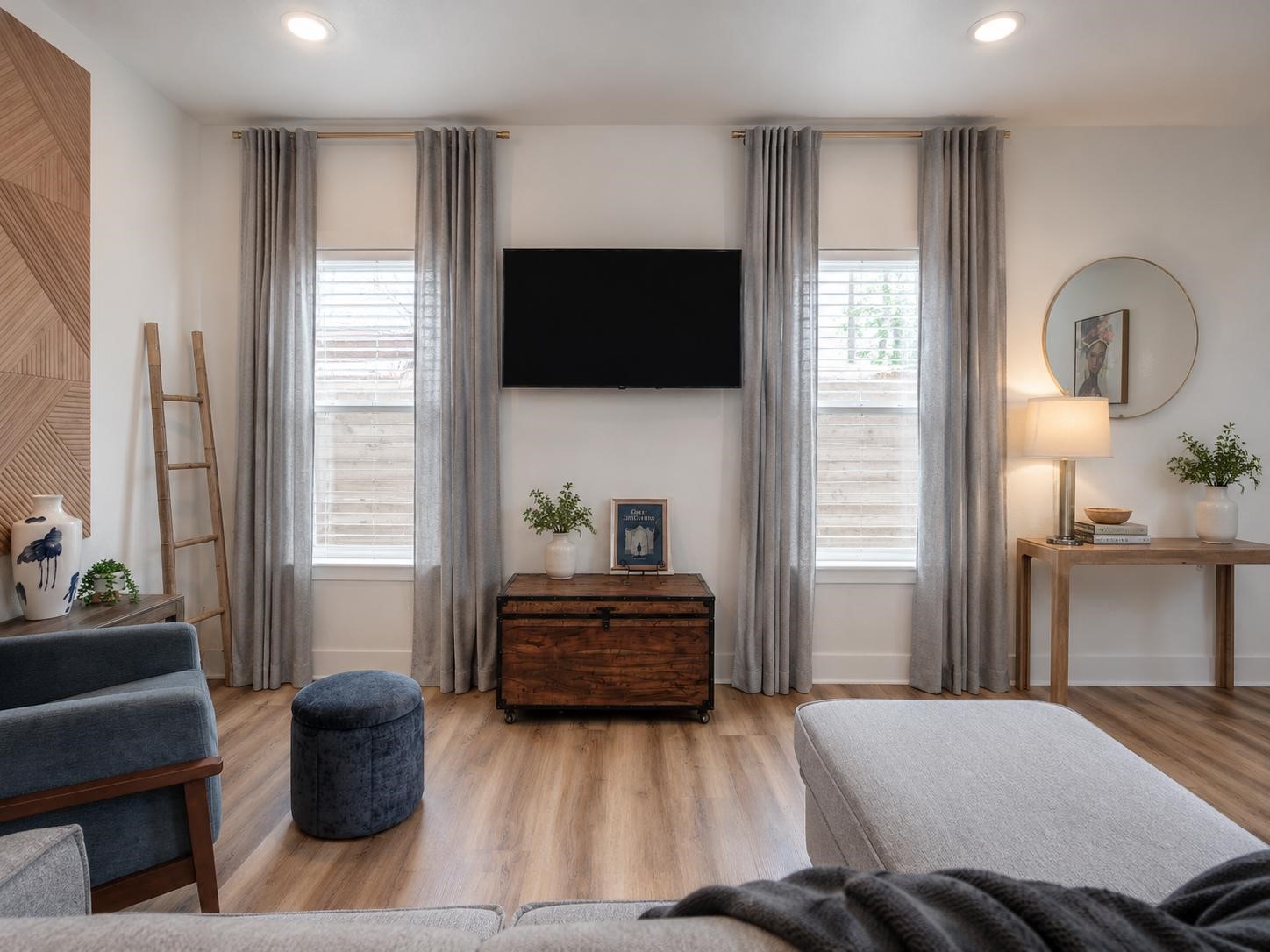 5407 Lee Street Houston, TX 77020 - Photo 4 of 17 This cozy living room features laminate wood flooring, two large windows with elegant curtains, a wall-mounted TV, and stylish decor. It's bright and inviting, perfect for relaxing and entertaining.
