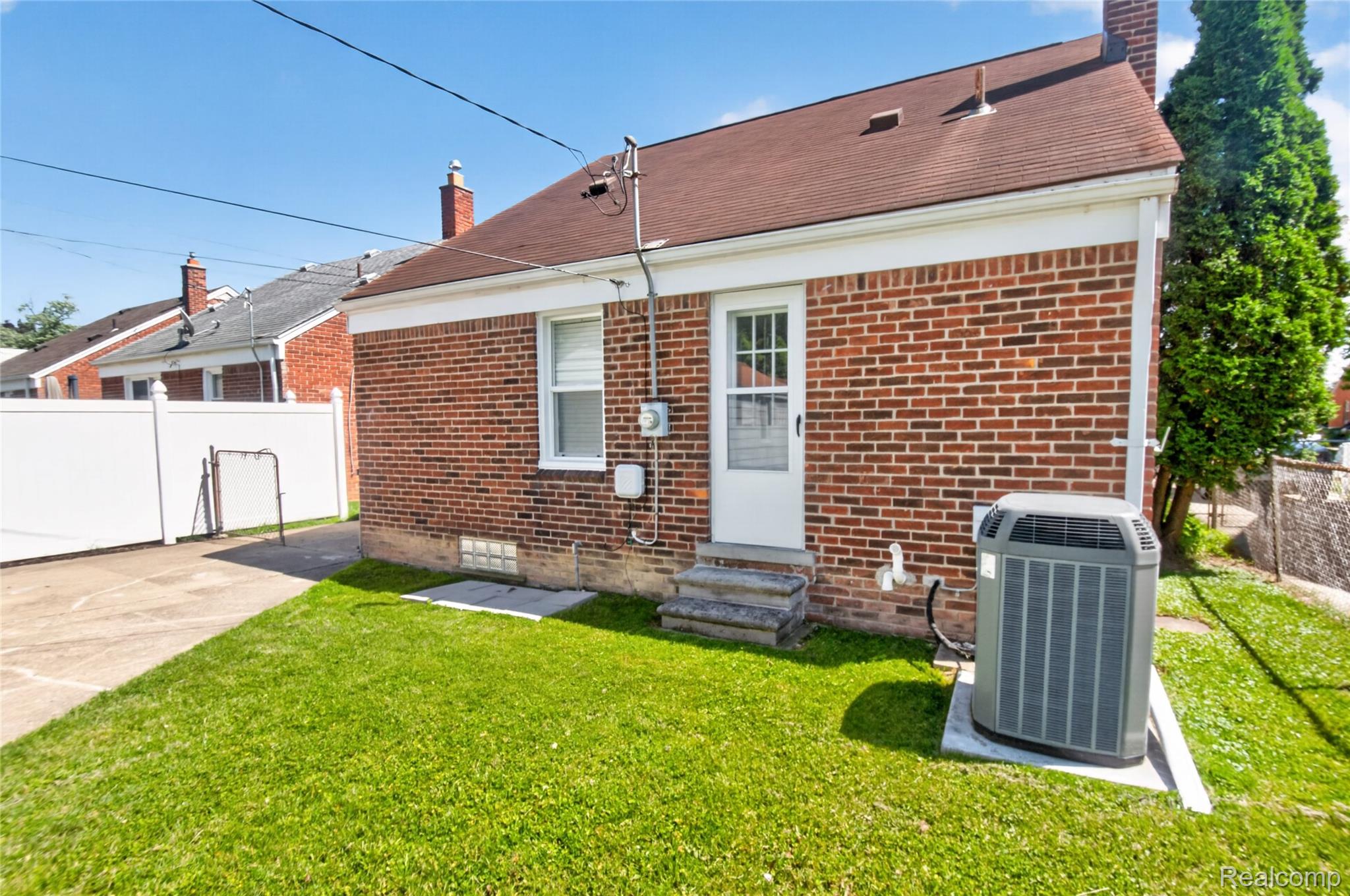 12972 Callender Street Southgate, MI 48195 - Photo 38 of 40 Brick exterior with a brown shingle roof, featuring a white rear entry door, and a dedicated concrete pad for the air conditioning unit